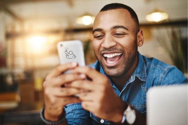 Um jovem negro, dando risada, olhando para o celular na mão.
